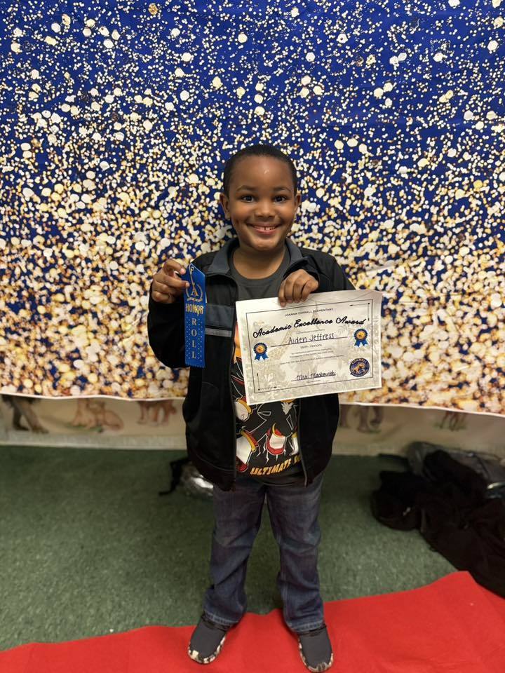 A student holding their Academic Excellence Award in front of a blue and gold backdrop.