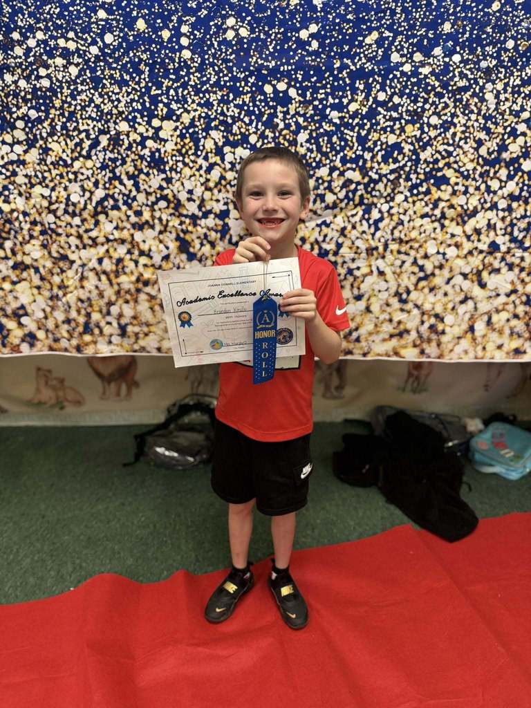 A student holding their Academic Excellence Award in front of a blue and gold backdrop.