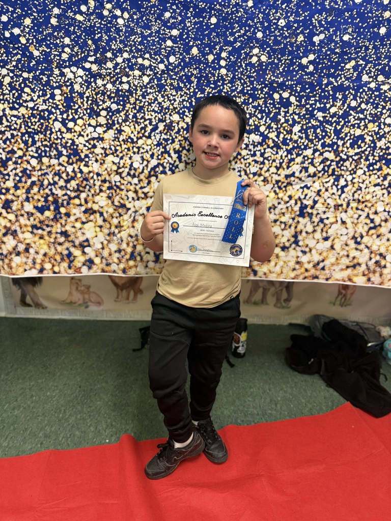 A student holding their Academic Excellence Award in front of a blue and gold backdrop.
