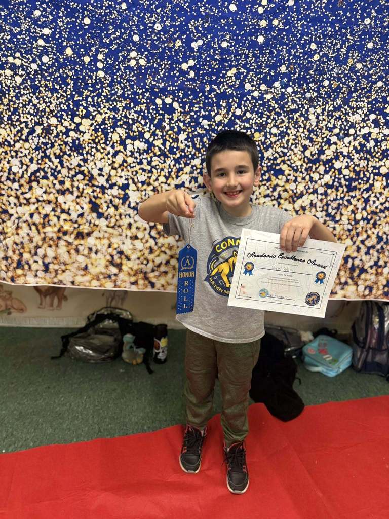 A student holding their Academic Excellence Award in front of a blue and gold backdrop.