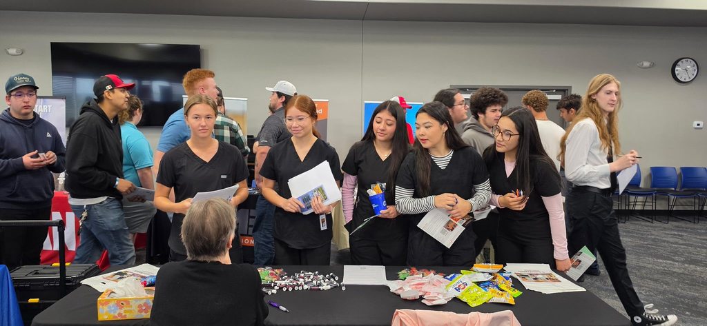 Several people gather around a table with various items, including papers and crafts, in an indoor room.