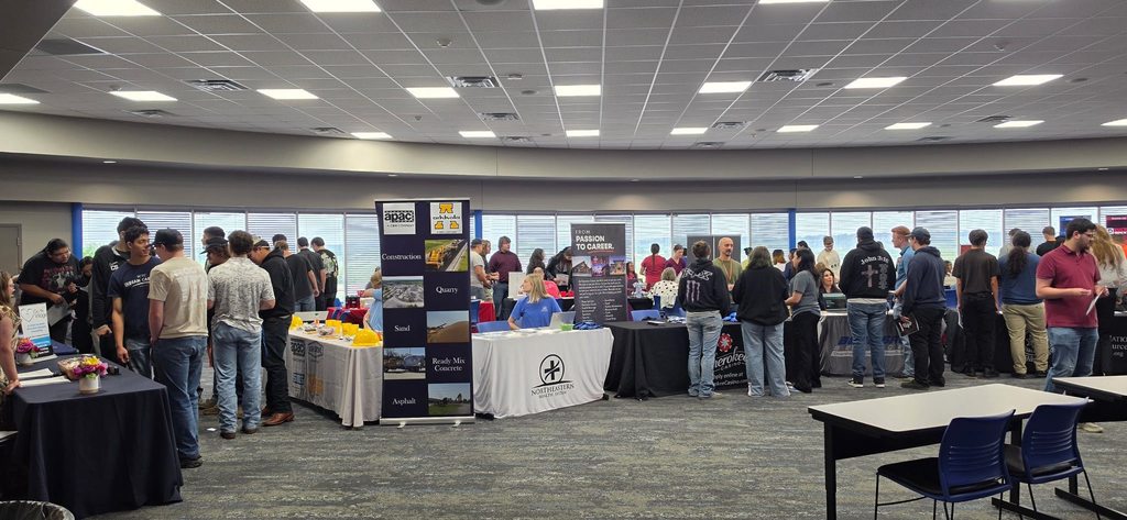 A group of people in a room with tables and chairs. They are gathered around tables with displays.