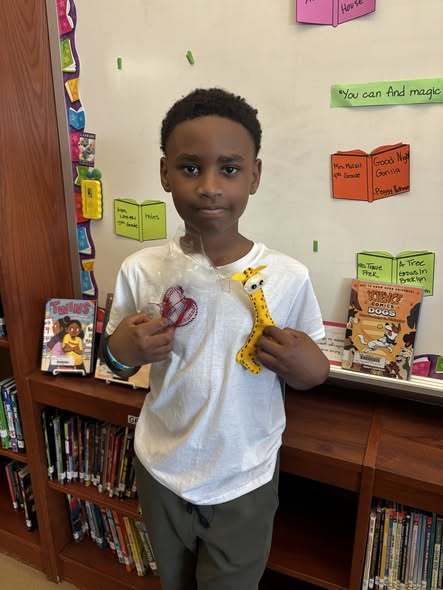 A Student holding yarn and a giraffe he made. 