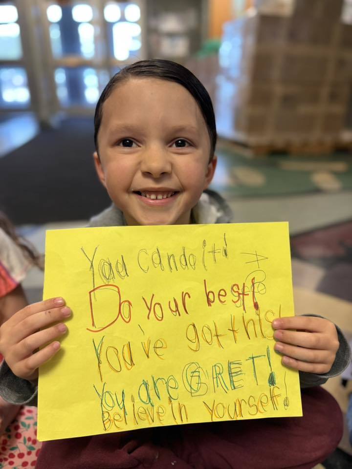 A Student standing with a poster she made to wish students good luck in her school.