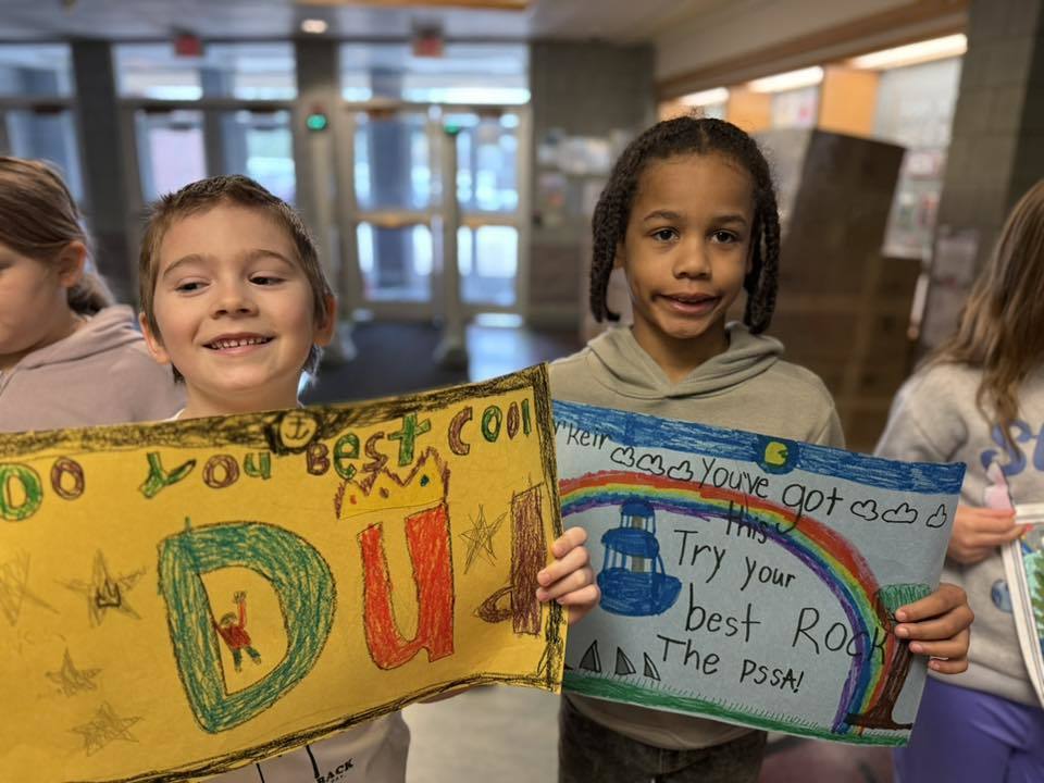 Students standing with posters they made to wish students good luck in their school.