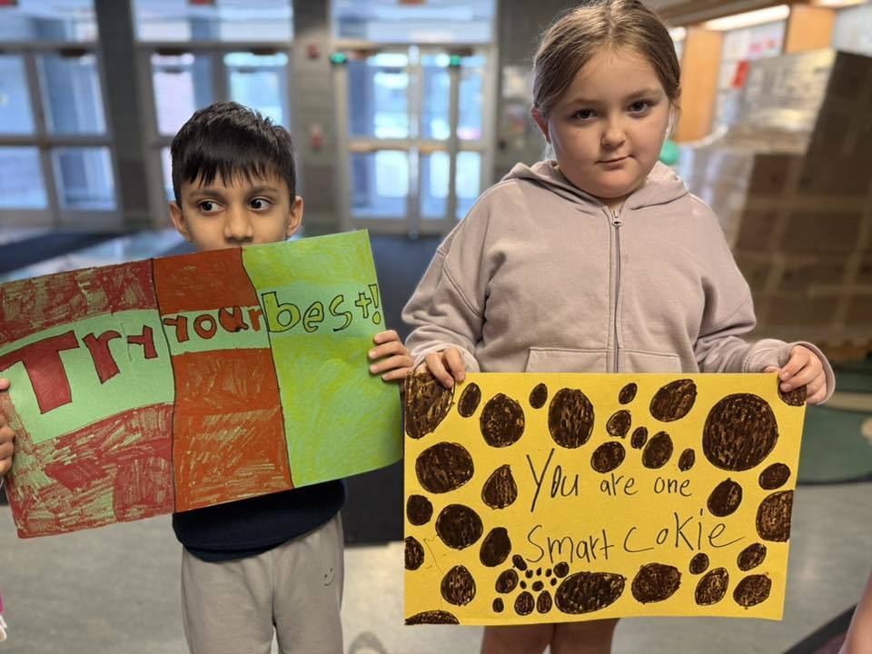 Students standing with posters they made to wish students good luck in their school.