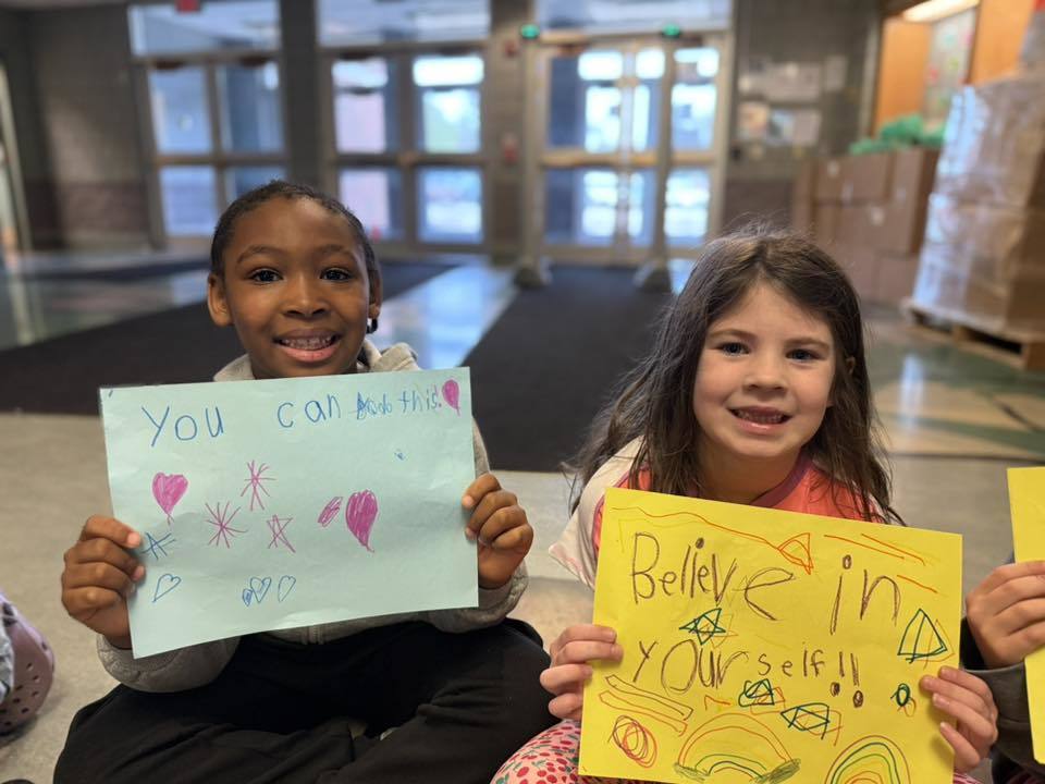 Students standing with posters they made to wish students good luck in their school.