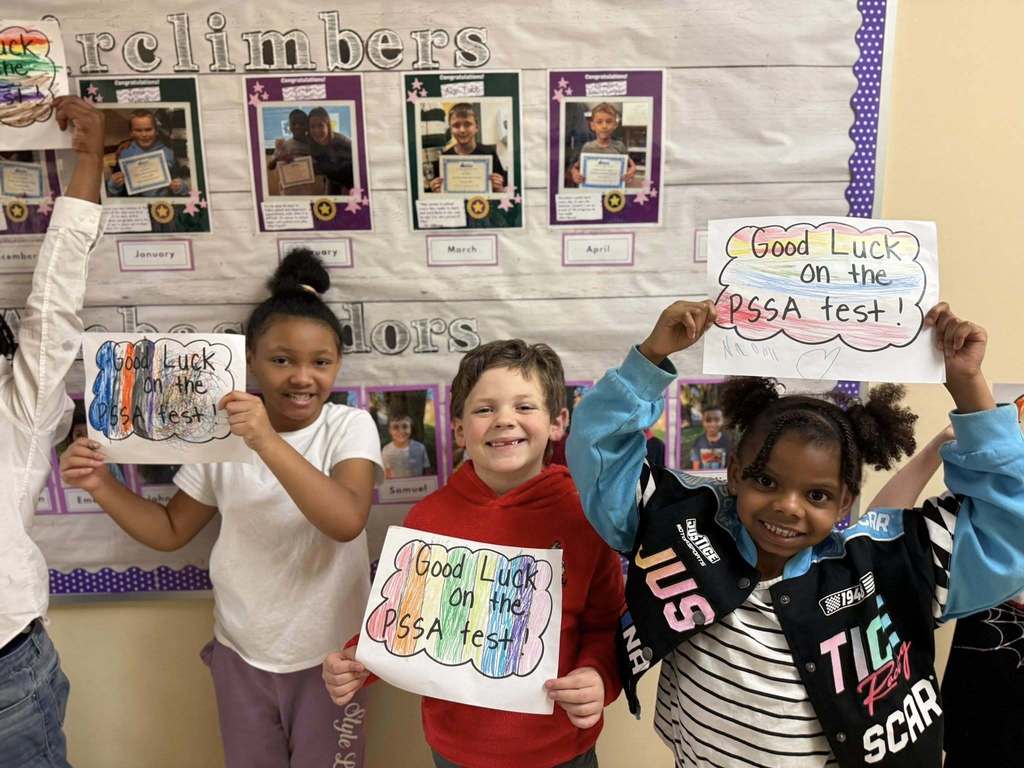 Students standing with posters they made to wish students good luck in their school.
