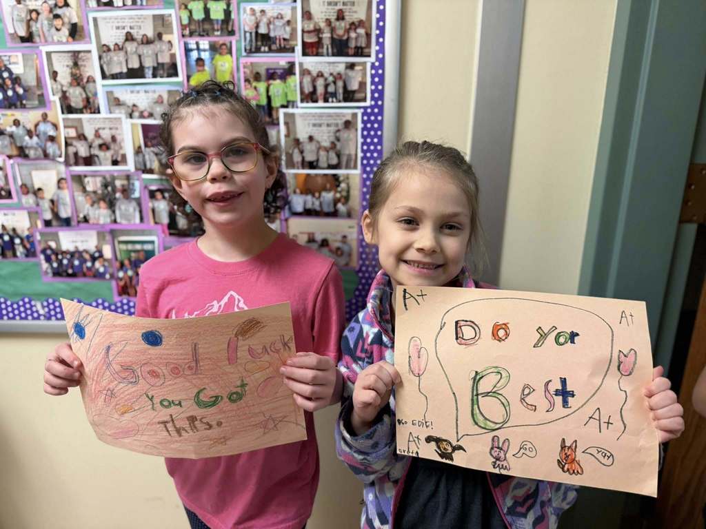 Students standing with posters they made to wish students good luck in their school.