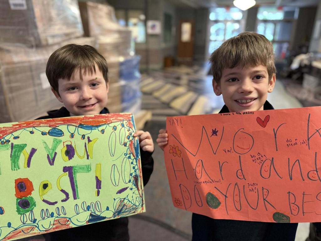 Students standing with posters they made to wish students good luck in their school.