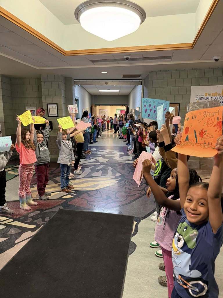 Students standing with posters they made to wish students good luck in their school.