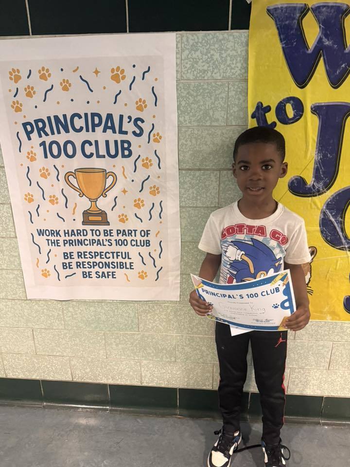 A student holding his Principal 100 Club award. 