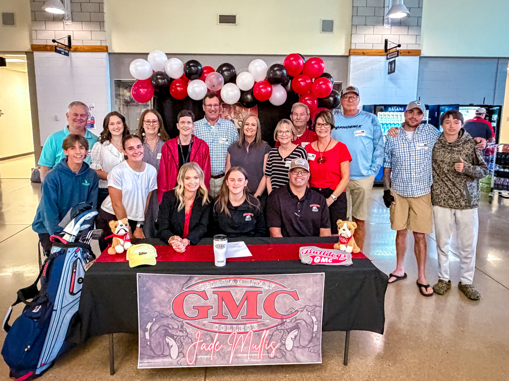A group of people in casual clothes stand behind a table with a banner that says "GMC Jack Miller."