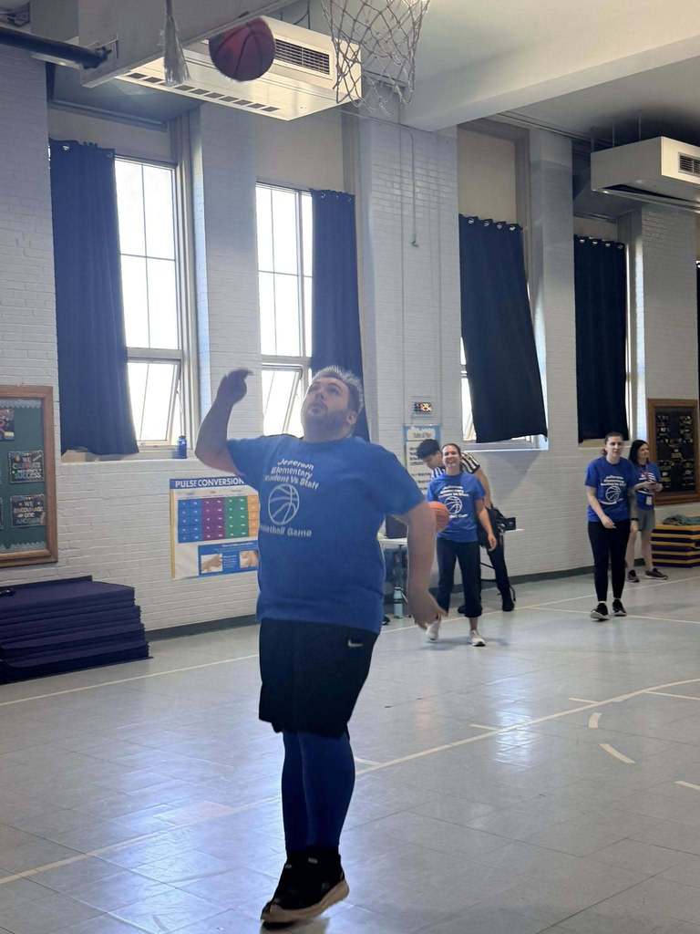 A staff member throwing a ball in the basketball hoop. 