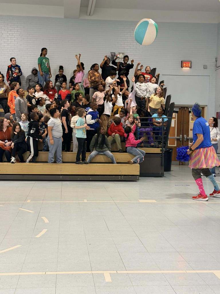 Students in the bleachers are reaching to hit a beach ball. 