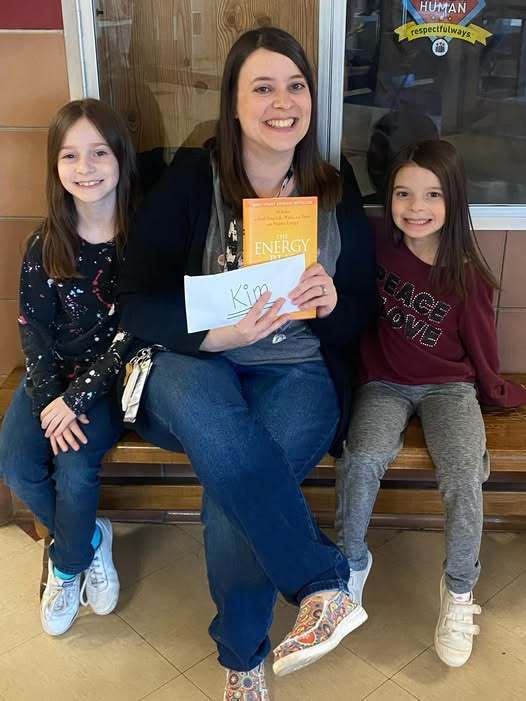 Two students sitting next to a women who is holding an envelope and yellow book. 