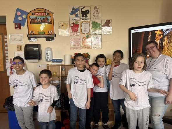 Students and staff wearing matching shirts while they pose in a classroom. 