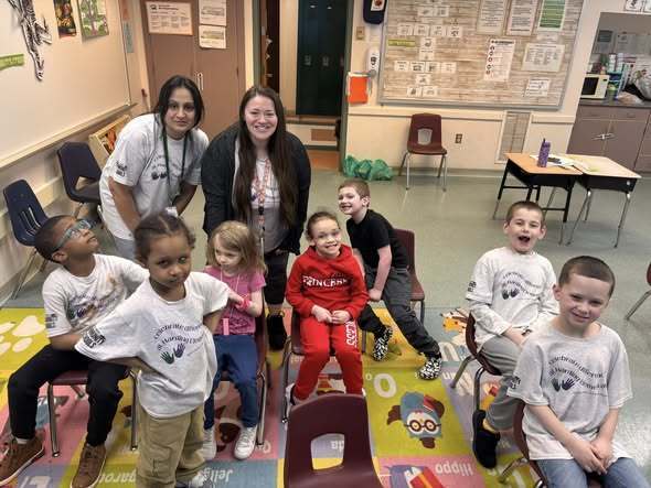 Students and staff wearing matching shirts while they pose in a classroom. 