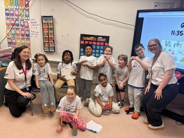 Students and staff wearing matching shirts while they pose in a classroom. 