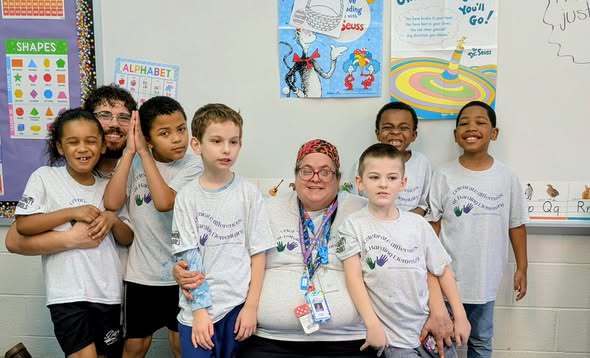 Students and staff wearing matching shirts while they pose in a classroom. 
