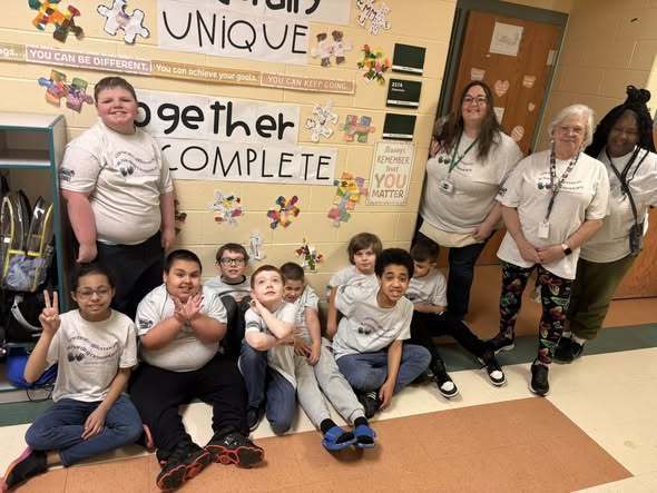 Students and staff wearing matching shirts while they pose in a classroom. 