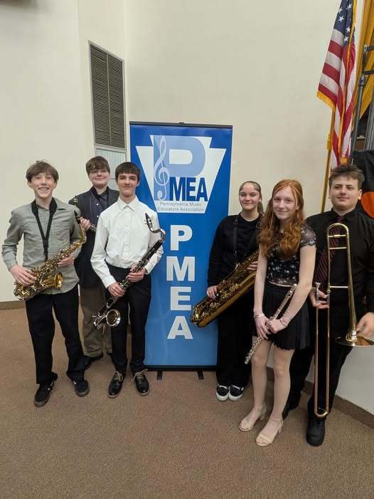 Students standing with their instruments next to a PMEA banner. 