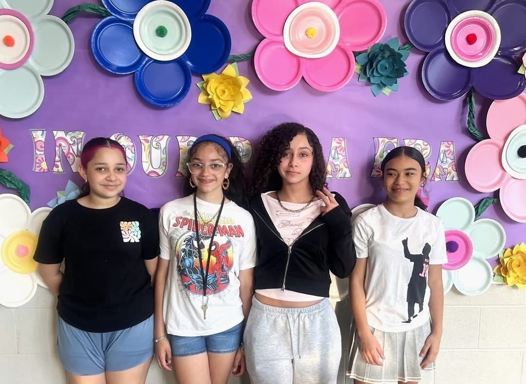 A group of middle school students standing in front of a colorful banner.
