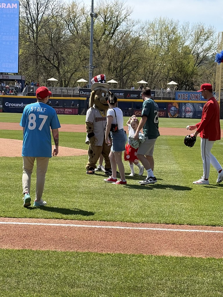 Student and baseball players making their way to the pitcher's mound.