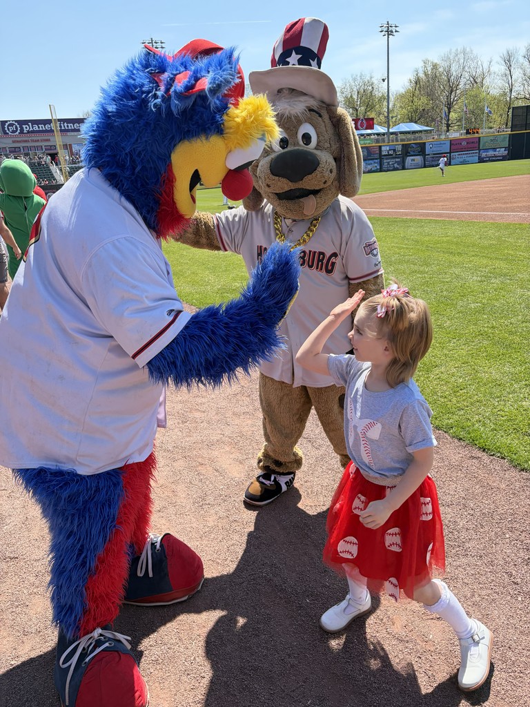 Student giving high fives to baseball team mascots.