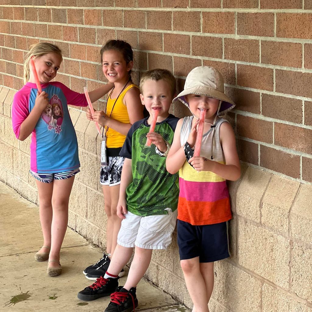 4 students eating popsicles in the shade smiling for the camera