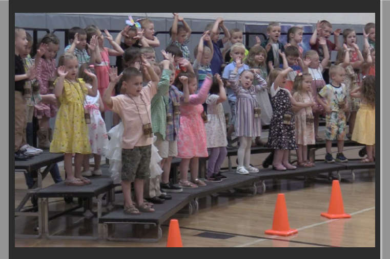 50 young students on risers singing. gymnasium