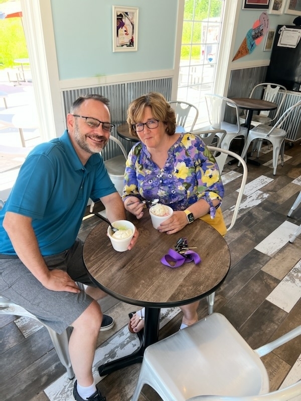 A man and a woman sit at a small round table and pose and smile while holding cups of ice cream