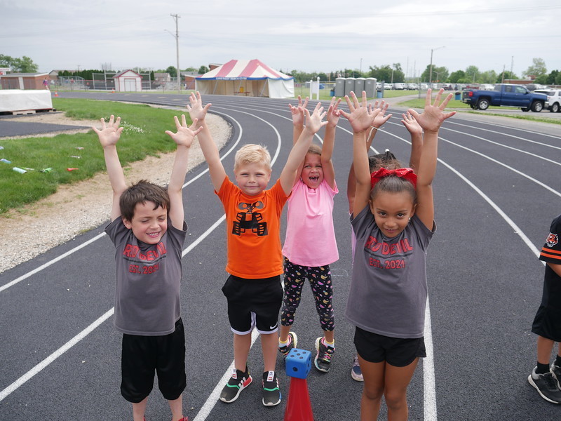 Kindergarten students raise their hands high to the sky. 