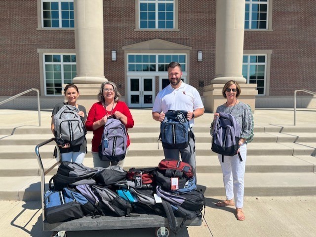 Counselors, Mr. Sherman, and DaySpringΕ Susan Stair standing in front of Legacy HS with donated backpacks for our students.
