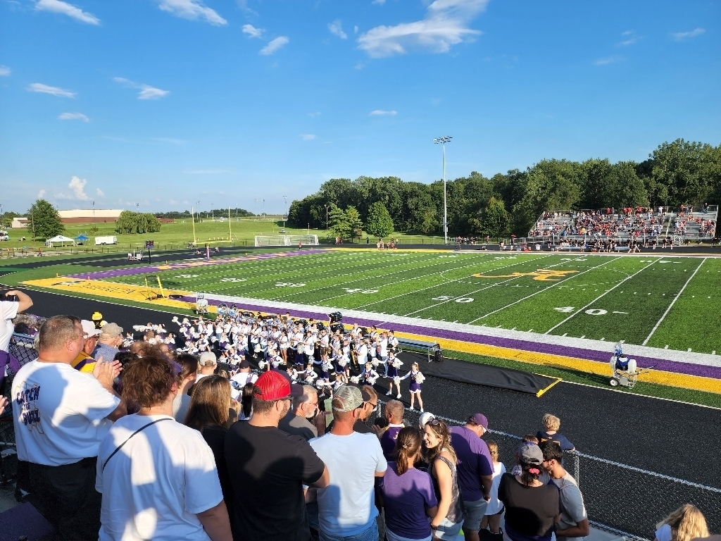 Cheerleaders and band stand on the track in front of the football field