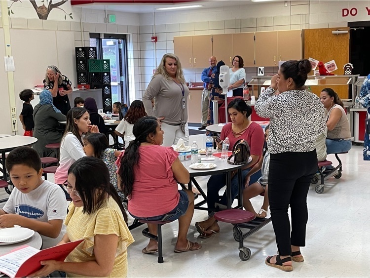 Families sitting at cafeteria tables listening to EL staff share information  