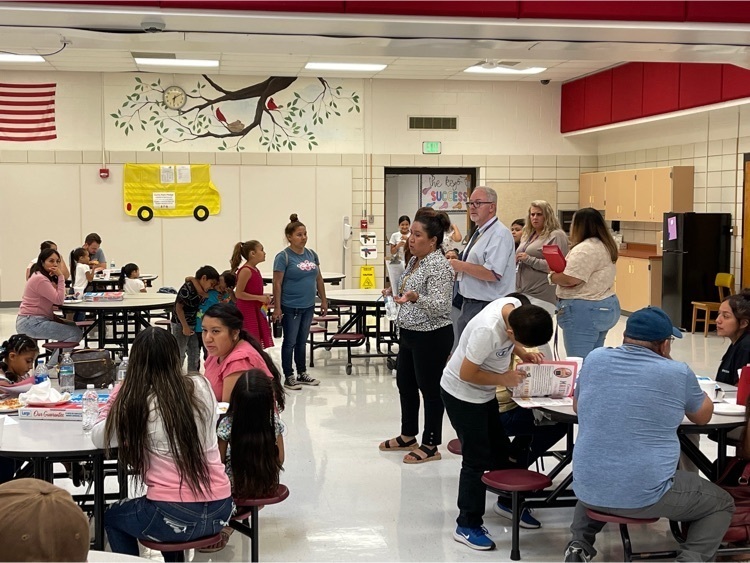 Families sitting at cafeteria tables listening to EL staff share information