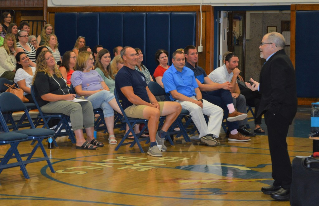 People sit in chairs  in an auditorium as a man speaks