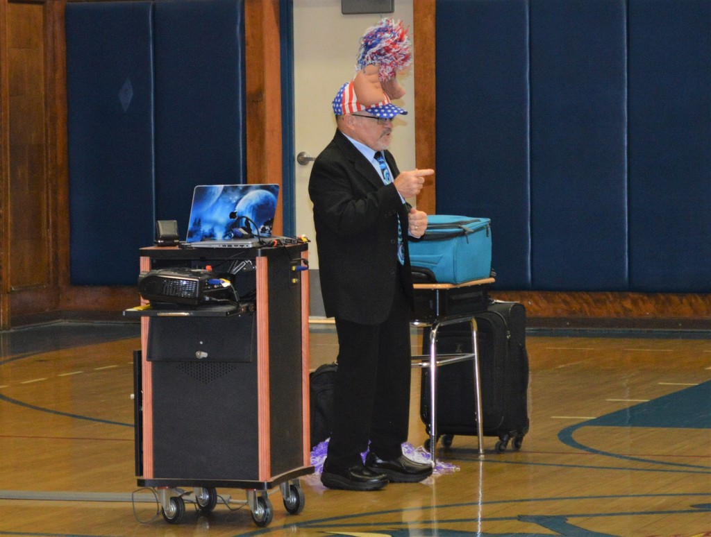 A man wears a red, white and blue, clapping hands hat during a presentation