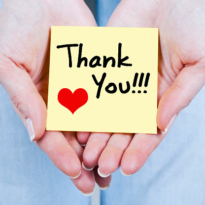 Thank you written on a post it with a heart in two hands.