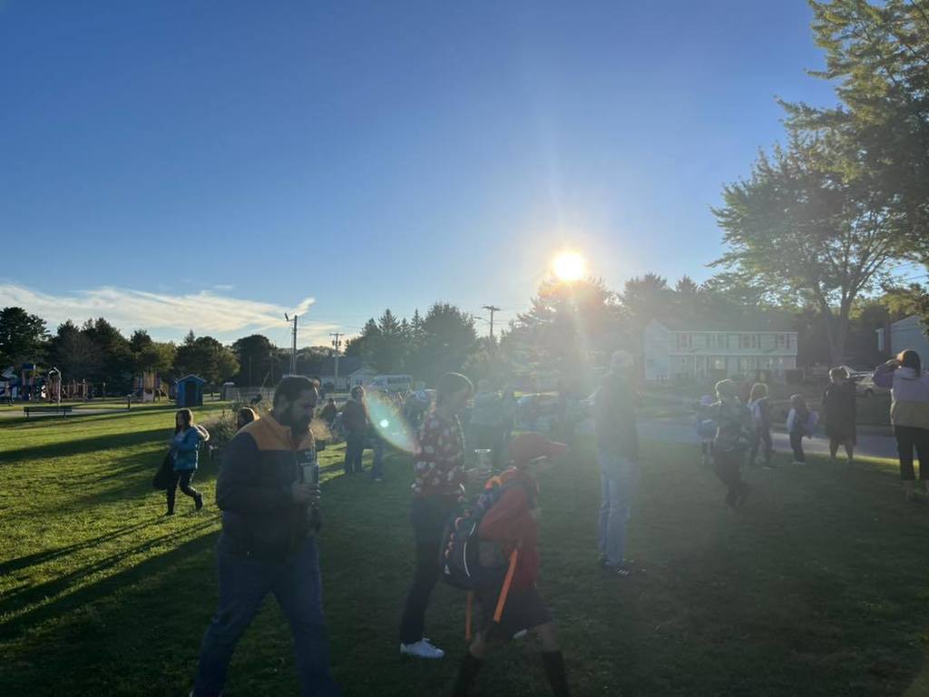 Sun over a group of families and staff waiting to walk to school