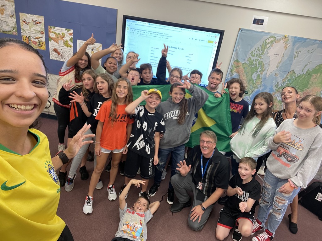 group of 6th grade students hold up a brazilian flag and wave to the camera