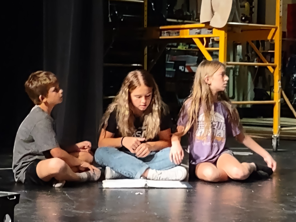 Sophomore sitting with two middle schoolers reading songs 