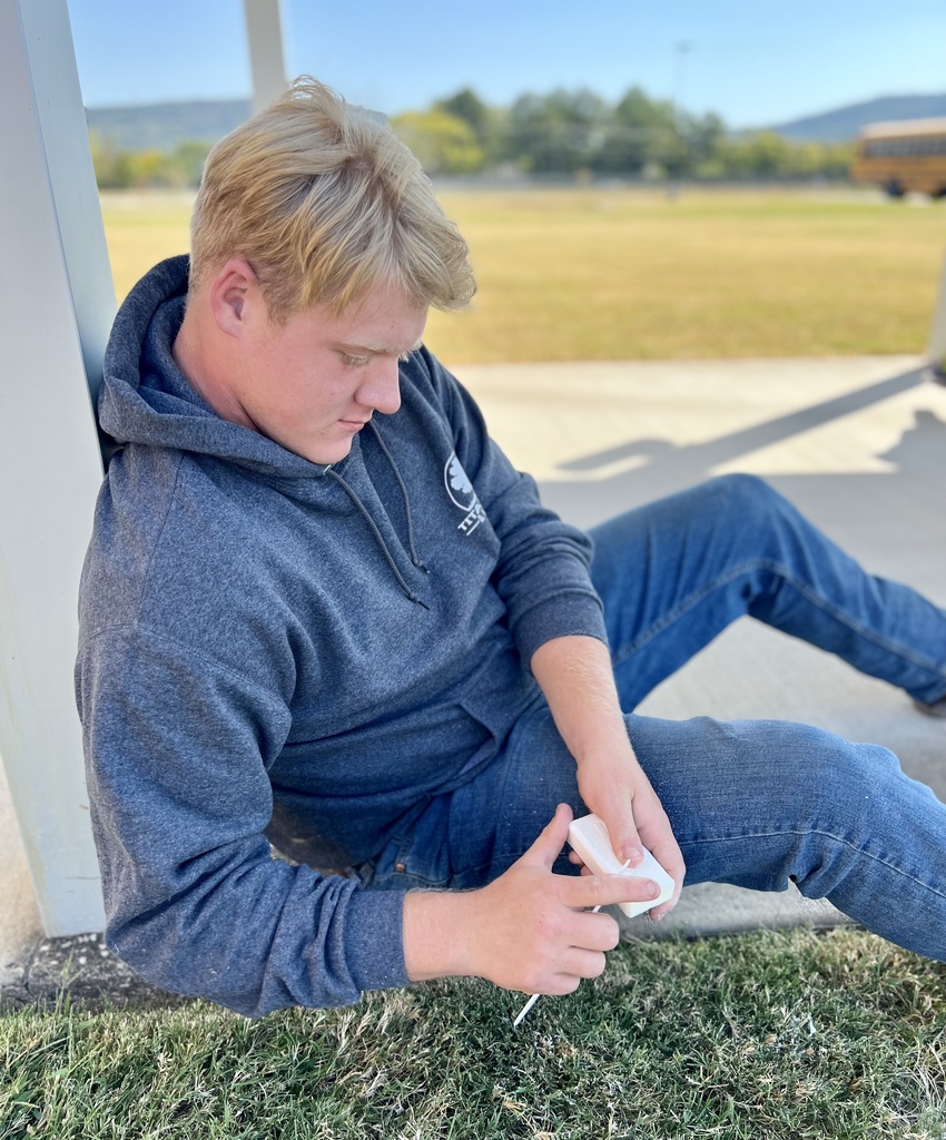 student sitting outside carving a bar of soap with a plastic knife