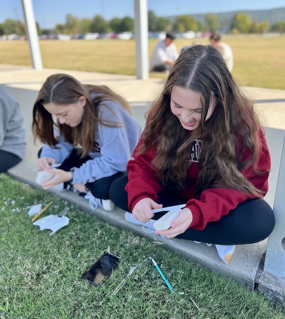 student sitting outside carving a bar of soap with a plastic knife