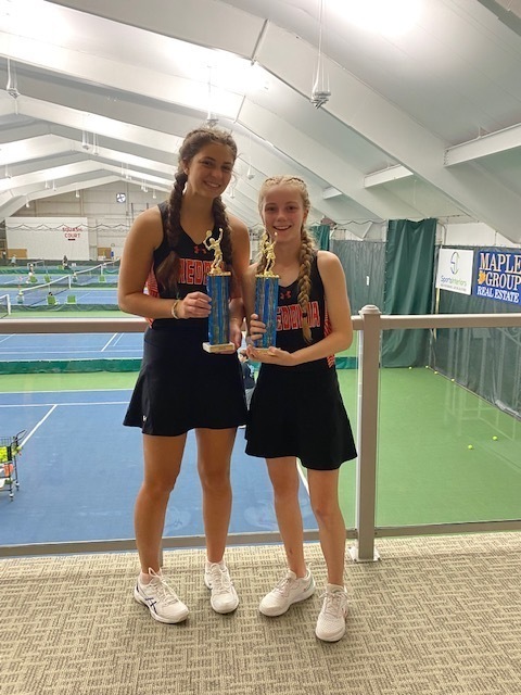 two girls tennis players hold trophies standing side by side