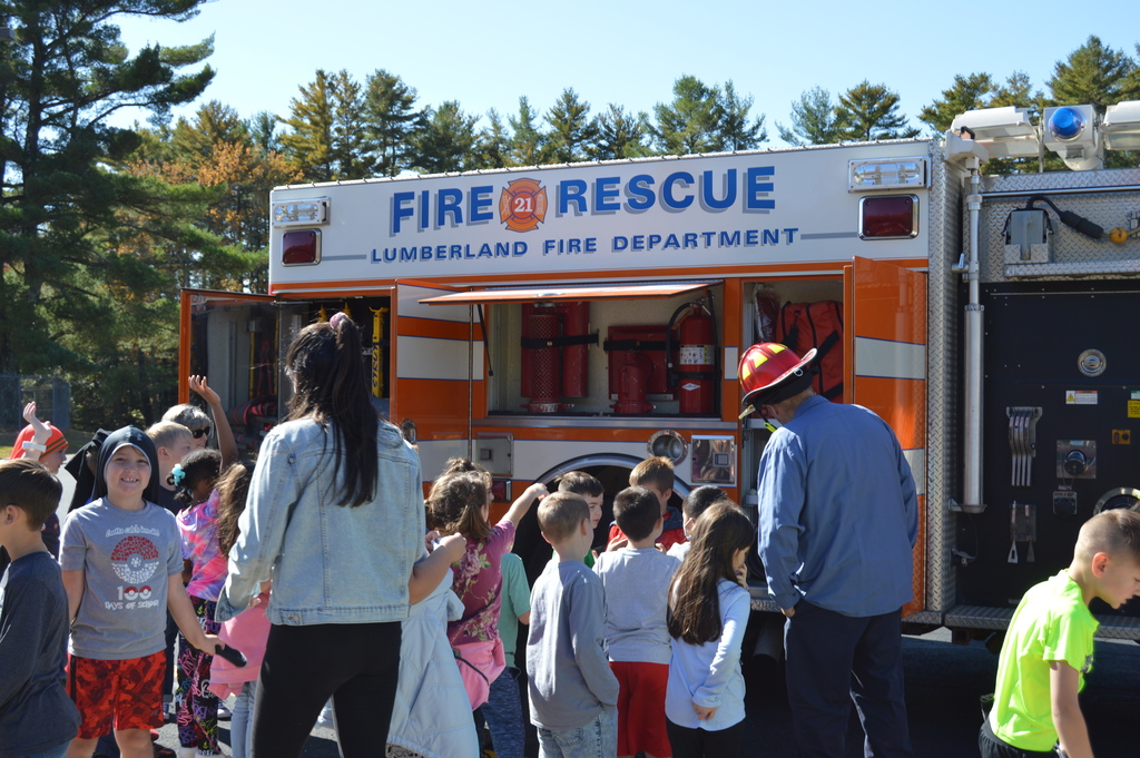 Lumberland Fire Department Fire Rescue truck is parked in the background while a fireman stands in front of the vehicle speaking to elementary school students.