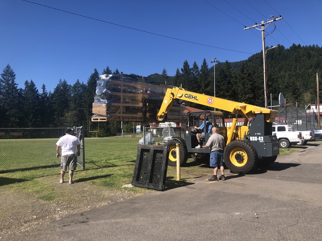 Unloading the new playground components. Lifting large pallet over fence and through a gate. 