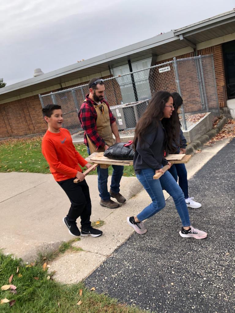 Students and teacher carrying a homemade wooden stretcher