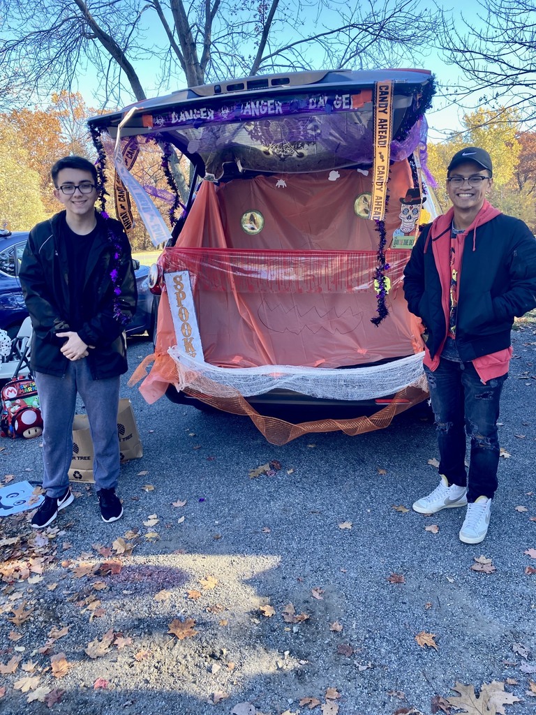 two students stand by an open van for trunk or treat